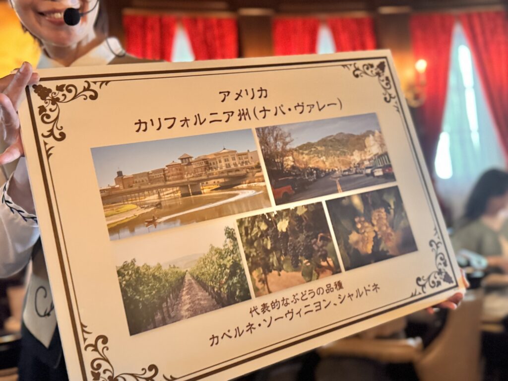 東京ディズニーシーのワインプログラムで紹介されたアメリカ・カリフォルニア州ナパ・ヴァレーのパネル。ぶどうの品種やワイナリーの写真が掲載され、キャストが説明している様子。